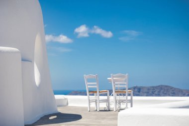 Santorini Adası, Yunanistan 'da beyaz mimari. Mavi deniz manzaralı, güneşli mavi gökyüzü olan Caldera 'da rahatla. Lüks yaz tatili, tatil. Çiftler için sandalyeler, romantizm, aşk, balayı yeri