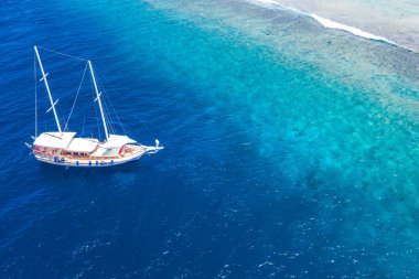 Maldivler adalarında yat gezisi. Beyaz yelkenlinin hava aracı görüntüsü demirli, kristal berrak turkuaz okyanus. Yaz sporu aktiviteleri, şnorkelle yüzme, dalış. Şaşırtıcı hava deniz doğa afişi