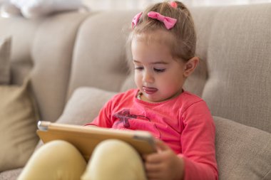 Tabletli ve kitap okuyan küçük bir kız.