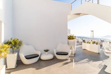 10.05.19 - Santorini, Yunanistan: Lüks oteldeki beyaz teras, Santorini Adası. Lüks bir restoran ve otel resepsiyonu. Beyaz iç mekan, sandalyeler ve masa, yumuşak mavi gökyüzü ve güneşli hava