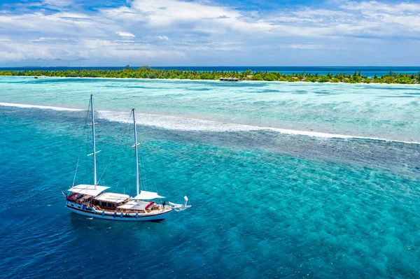 Sailing yacht in Maldives islands. Aerial drone view of white sailboat anchored, crystal clear turquoise ocean. Summer recreational sport activity, snorkeling, diving. Amazing aerial sea nature banner