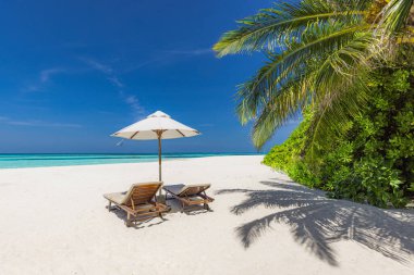 İki ahşap şezlong ve şemsiyenin el değmemiş tropik bir plajda yatay görüntüsü.