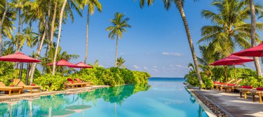 Palmiye ağaçları, şezlonglar ve yüzme havuzunun yanındaki kırmızı şemsiyeler üzerinde yükseliyor..