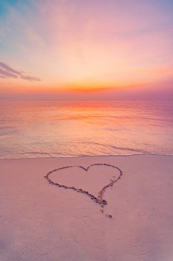 Gün batımında canlı bir gökyüzünün altında kumsalın ıslak kumlarında çizilmiş basit bir kalp şekli..