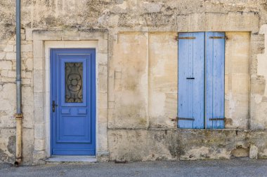 Canlı mavi kapısı ve uygun pencere panjurları olan eski bir taş duvara yakın plan..