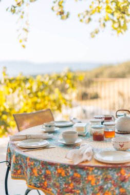 Kahvaltı masası verandada, güneşli, bulanık üzüm bağları ve tepelere bakıyor..