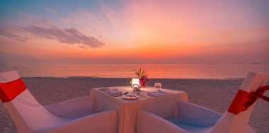 Gün batımında kumsalda renkli bir gökyüzünün altında özel bir yemek masası.