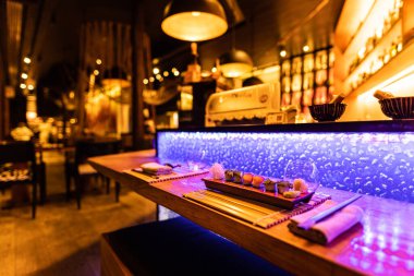 Suşi tezgahında loş bir Japon restoranında mavi aksanlı ışıklar ve asılı lambalar..