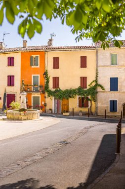 Taş bir çeşme, heykel ve parlak renkli Akdeniz binalarıyla büyüleyici köy meydanı..