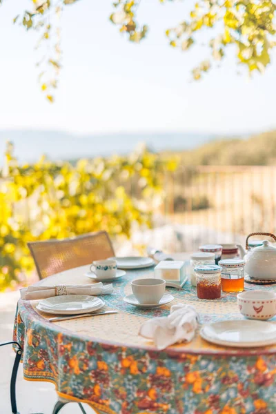 Kahvaltı masası verandada, güneşli, bulanık üzüm bağları ve tepelere bakıyor..