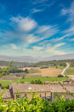 Yuvarlanan tepelerin panoramik manzarası, lavanta tarlaları, vadi, yol ve köy çatıları.