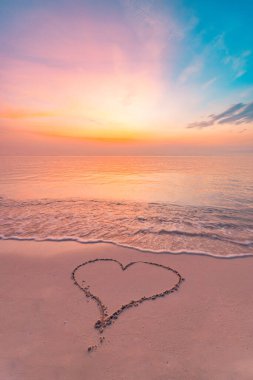 Gün batımında canlı bir gökyüzünün altında kumsalın ıslak kumlarında çizilmiş basit bir kalp şekli..