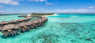 Suüstü bungalovları durgun su üzerinde dramatik pembe ve turuncu bir tropikal gün batımına karşı gölgelenmiştir..