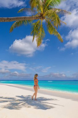 Beyaz bir kumsalda, palmiye ağacının altında duran bir kadın okyanusa bakıyor..