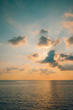 Sakin turkuaz su üzerinde tropik günbatımı, pastel bulutlu gökyüzü..