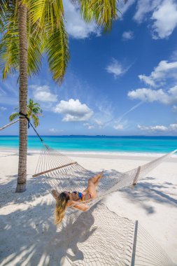Hamakta dinlenen bir kadın el değmemiş, beyaz bir tropik kumsalda..