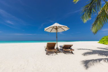 Tropik bir sahilde iki şezlong ve şemsiye..