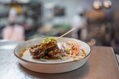 Jöleli tavuk şişleri lahana salatası ve profesyonel bir mutfak ortamında serpiştirilmiş sosla kaplıdır..