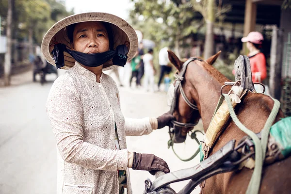 Vietnamesische Frau trägt einen konischen asiatischen Hut, der neben einem Pferd steht — Stockfoto