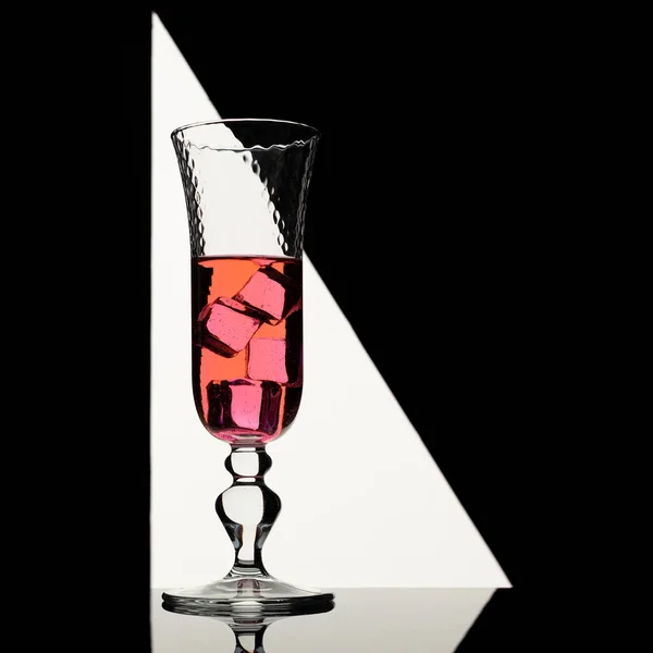 Pink drink in elegant glass with ice cubes backlit in geometric shaped light