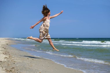 Çiçekli elbiseli genç kız denizin ve mavi gökyüzünün arka planında donup kaldı.