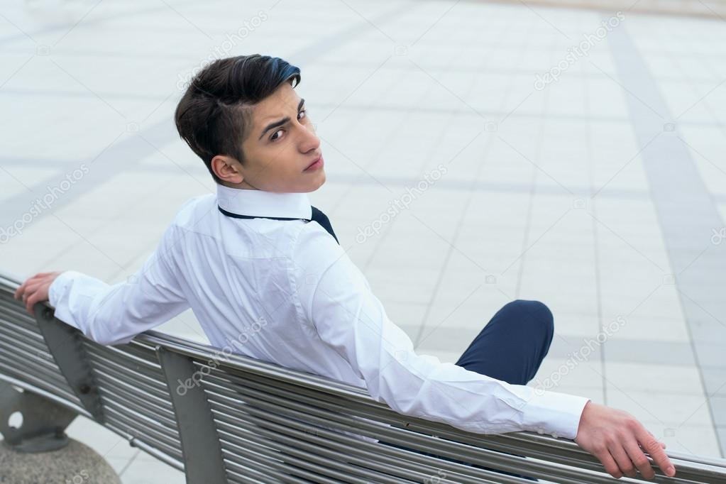 trandy teen guy sits on a bench