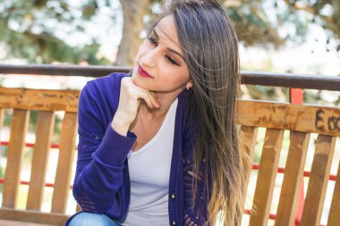 parkta bir bankta oturan genç dalgın esmer kadın