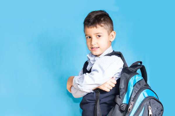happy first-grader boy with a school satchel on his back on a blue background