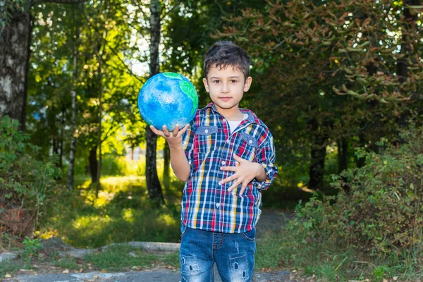 学齢期の少年は自然を背景に地球のモデルを持っています ストック写真