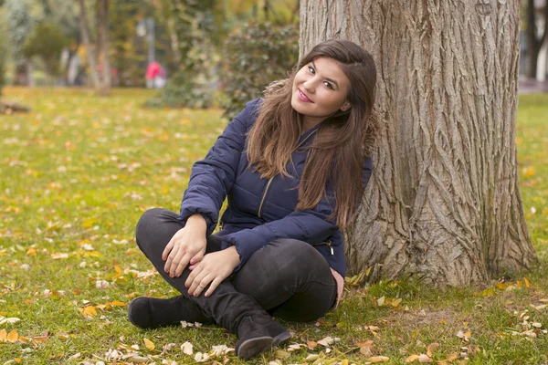 Una mujer joven se sienta cerca de un árbol — Foto de Stock