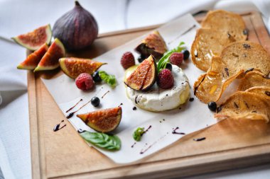 Ahşap tahtaya serpiştirilmiş incirler, peynirli ve bruschetta soslu, yakın plan.