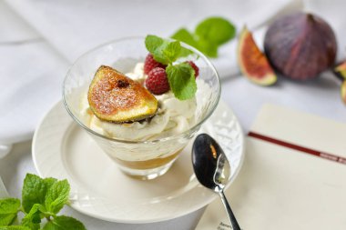 İncir ve nane yapraklarıyla süslenmiş cam bir bardakta panna cotta. 