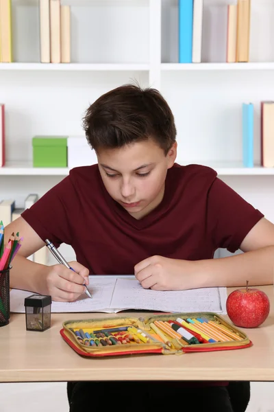 Jovem estudante escrevendo em seu caderno de exercícios na escola — Fotografia de Stock