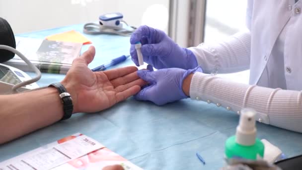Крупним планом анонімний лікар-терапевт в латексних рукавичках, що пробиває палець і приймає аналіз крові від пацієнта під час роботи в сучасній лікарні — стокове відео