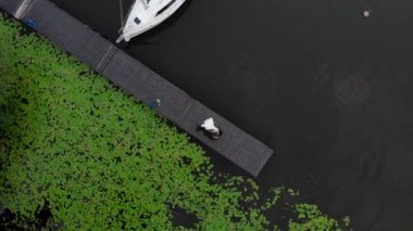 İnsansız hava aracı görüntüsü yukarıdan aşağıya, gelin ve damat nehir kıyısındaki küçük bir köprüde uzanıyor.