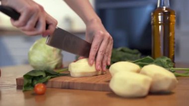 Kameranın Dolly görüntüsü. Tahta kesme tahtasında patates dilimlemek. Patates doğrayan bir kadın..