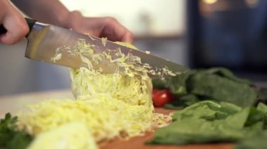 Kadınların elleri, mutfak bıçağıyla tahta kesme tahtasıyla taze beyaz lahana kesiyor..