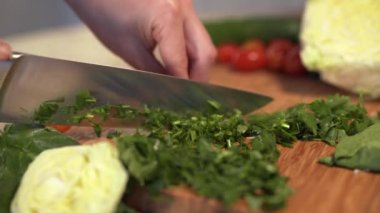 Kadın elleri mutfak bıçağıyla tahta kesme tahtasıyla taze dereotu ve maydanoz kesiyor..