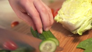Kameranın Dolly görüntüsü. Kadınların elleri mutfak bıçağıyla tahta kesme tahtasıyla taze salatalık kesiyor. Sağlıklı beslenme. Dilimlenmiş salatalık.