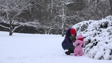 Anne ile kız bebek karla kaplı kış bahçesinde iyi eğlenceler. 4k