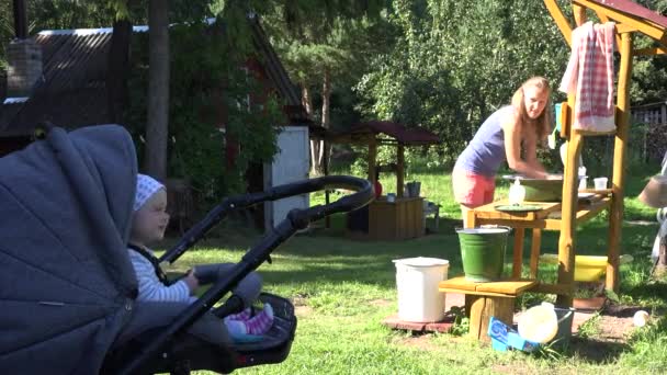 Baby isst Knacker im Kinderwagen und Dorfmutter kommuniziert beim Waschen. — Stockvideo