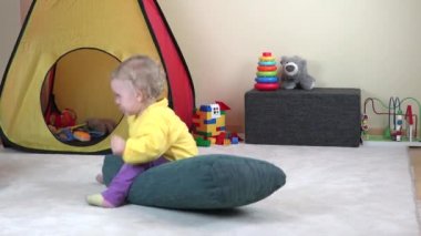 Neşeli bebek kız evde halı üzerinde büyük mavi yastık binmek.