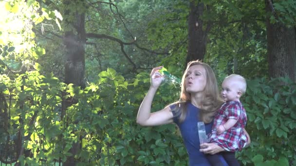 Nanny vrouw klap zeepbellen en babymeisje kijken naar hen in de prachtige zonsondergang licht in park. — Stockvideo