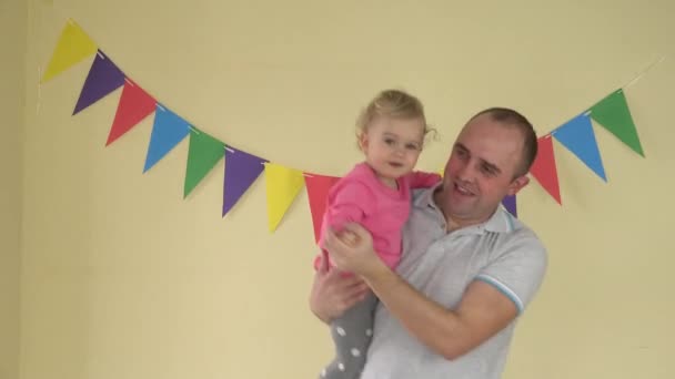 黄色の背景と色鮮やかな旗の上で踊って女の赤ちゃんとお父さんお母さん — ストック動画