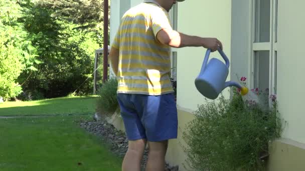 Mannelijke tuinman boer man met blauwe gieter water bloempot op de vensterbank. — Stockvideo