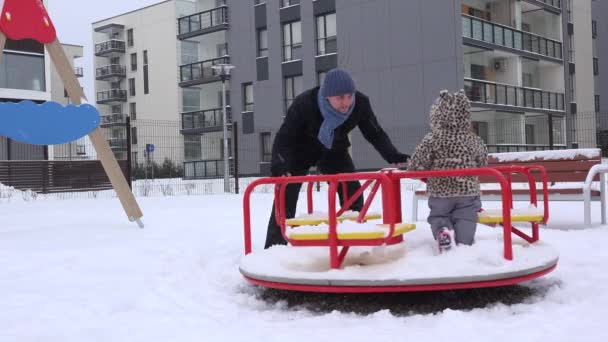 Apa és baba lány spin a szabadtéri játszótéren, udvaron téli kör. — Stock videók