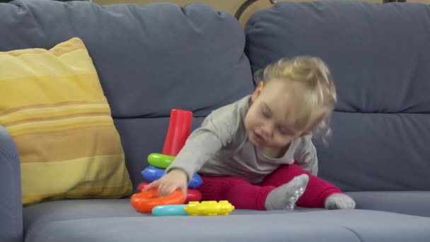 Baby Mädchen sitzt auf Sofa spielen Pyramide Turm. Frühpädagogisches Konzept. — Stockvideo