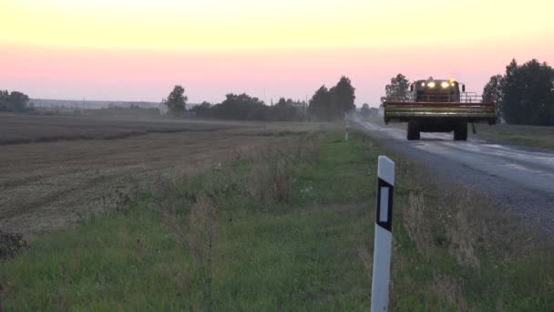 Tunga combine harvester maskin körning på väg väg från jobbet i fält på kvällen sunset. 4k — Stockvideo