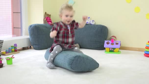 Söt blond barn girl rida stora kudde på golvet och falla ner hemma. — Stockvideo