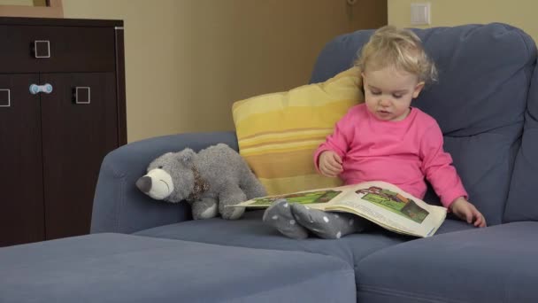 Kleinkind blättert Buchseiten mit bunten, interessanten Bildern im Sitzen — Stockvideo